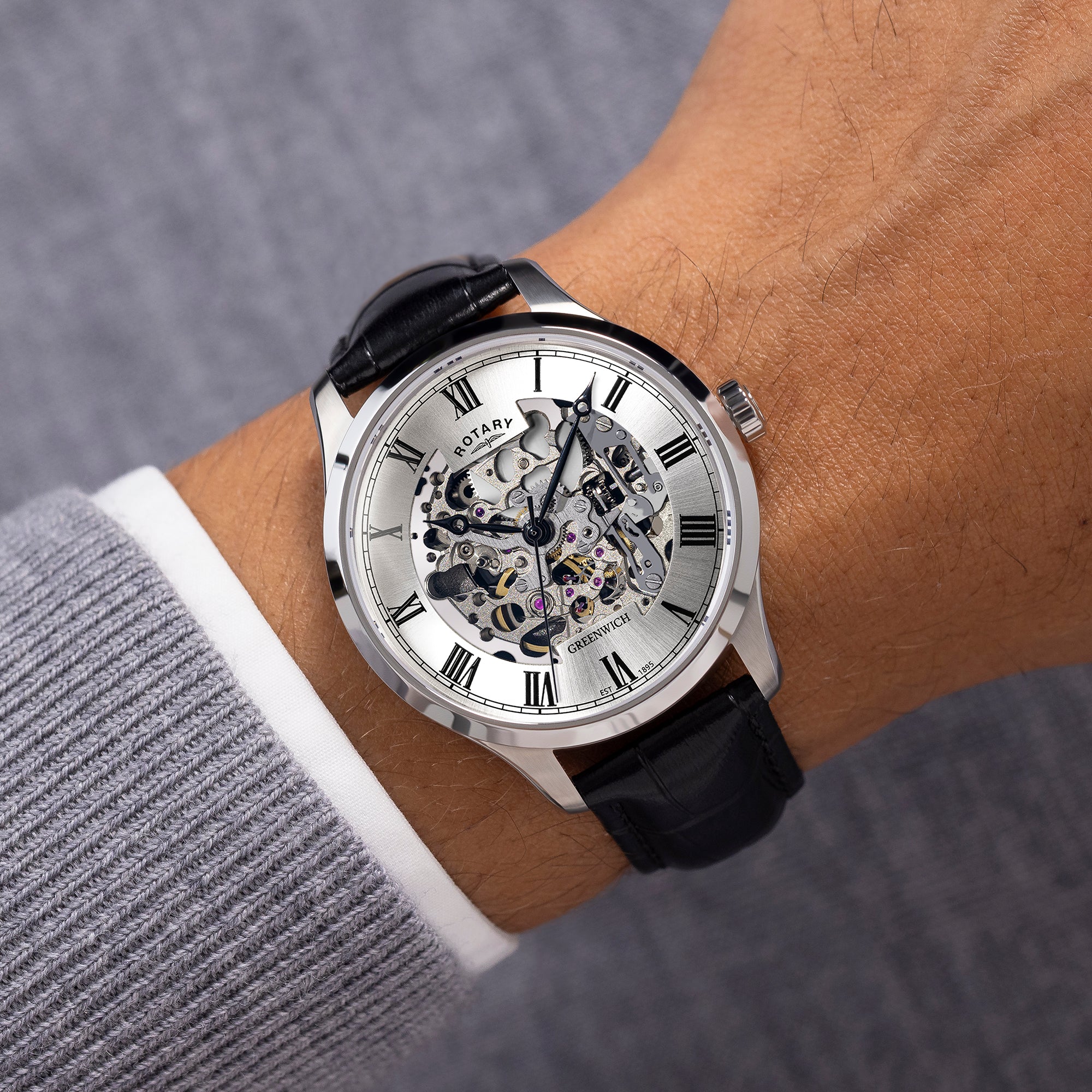 Watch with a black strap and silver case on a wrist, against a neutral background